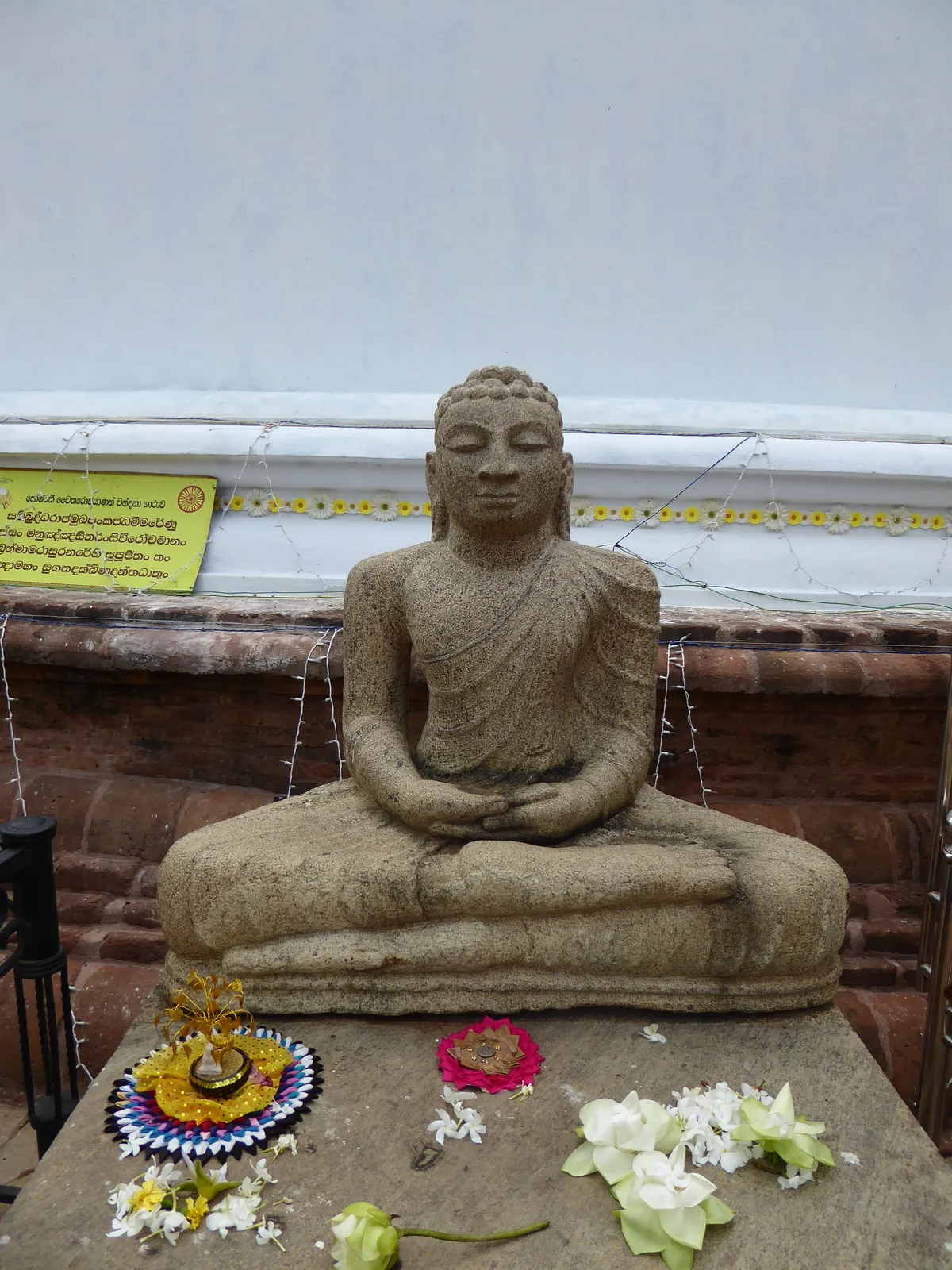 Statua del Buddha in meditazione adornata con offerte di fiori bianchi e petali, come avviene nelle pagode durante la festa di Visak Bochea