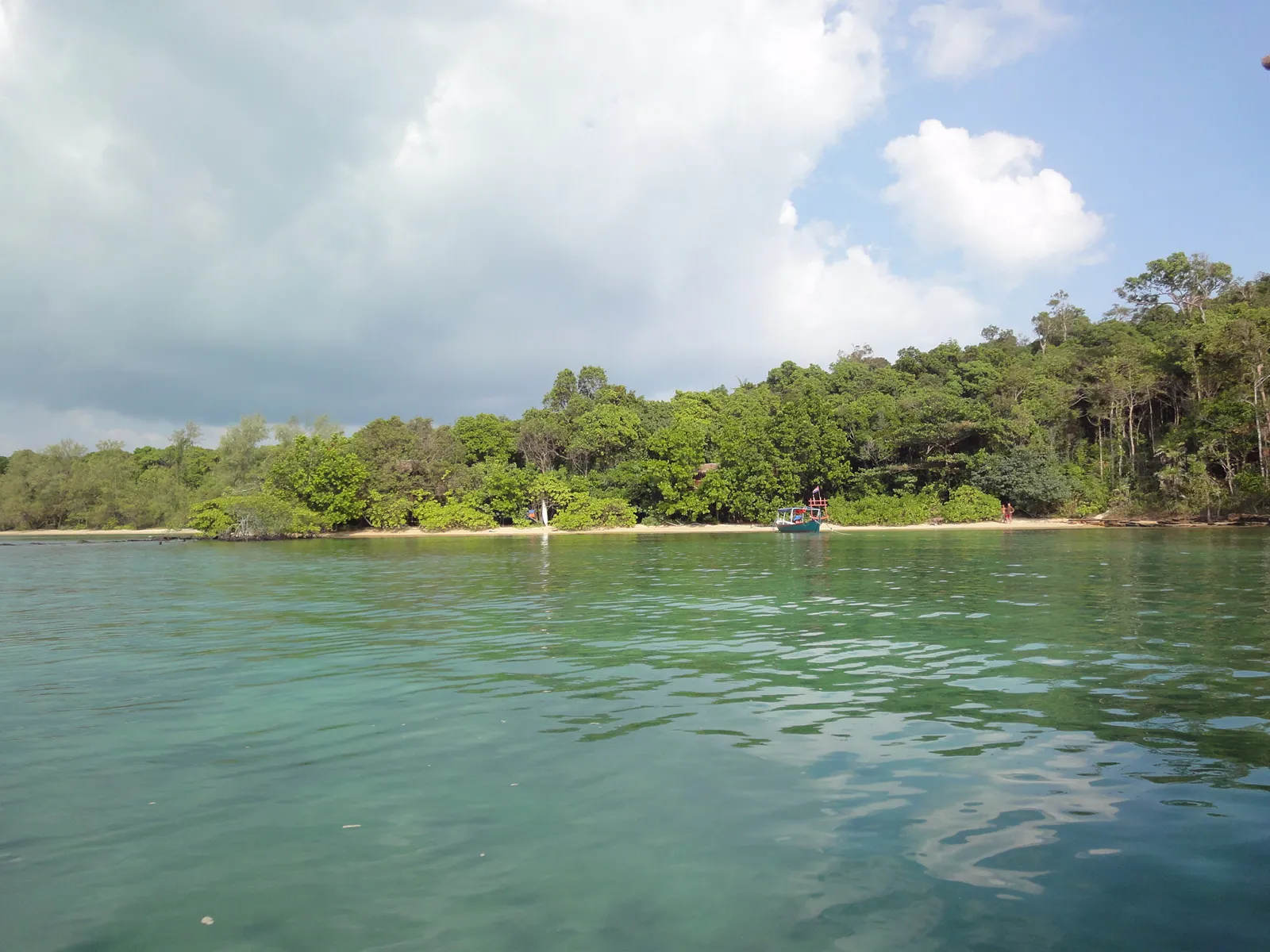 La costa selvaggia di Koh Ta Kiev La costa di Koh Ta Kiev con la giungla che arriva fino alla spiaggia e una barca tradizionale, Cambogia
