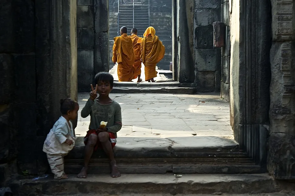 due bambini posano per una fotografia all'interno di un tempio ad Angkor, sullo sfondo dei monaci con le loro vesti color zafferano