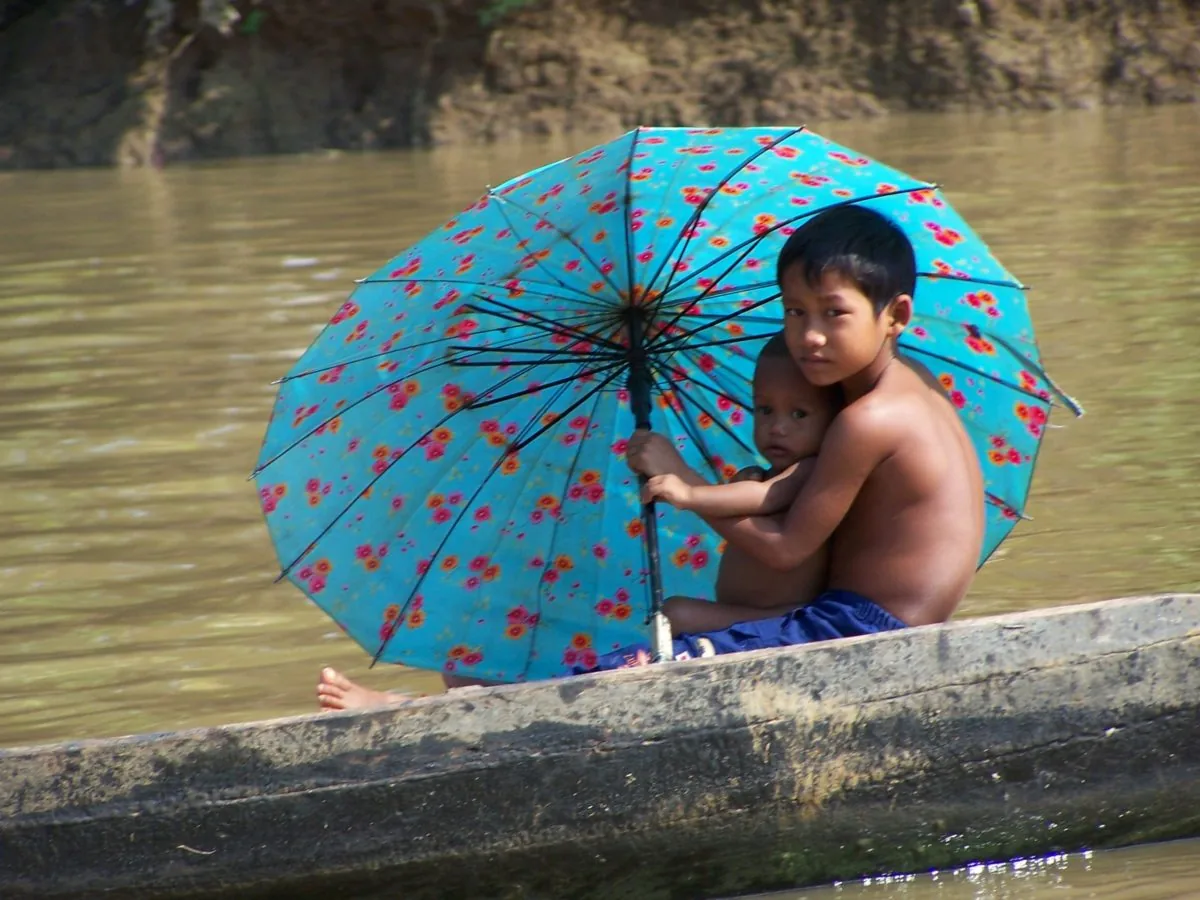 Villaggi dimenticati, l'esperienza di Koh Pek due bambini si riparano dal sole con un ombrello in riva al fiume