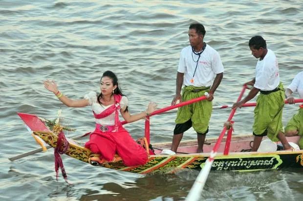 due vogatori e una donna in costume tradizionale a bordo di una barca durante una regata storica del Festival dell'Acqua in Cambogia due vogatori e una donna in costume tradizionale a bordo di una barca durante una regata storica del Festival dell'Acqua in Cambogia