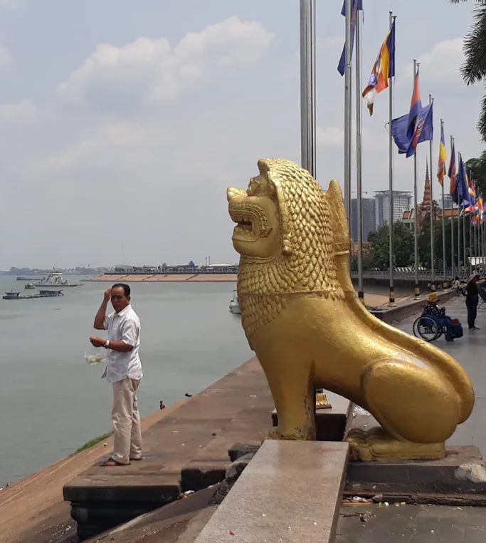 un uomo accanto alla statua di un leone dorato sul lungofiume a Phnom Penh un uomo accanto alla statua di un leone dorato sul lungofiume a Phnom Penh
