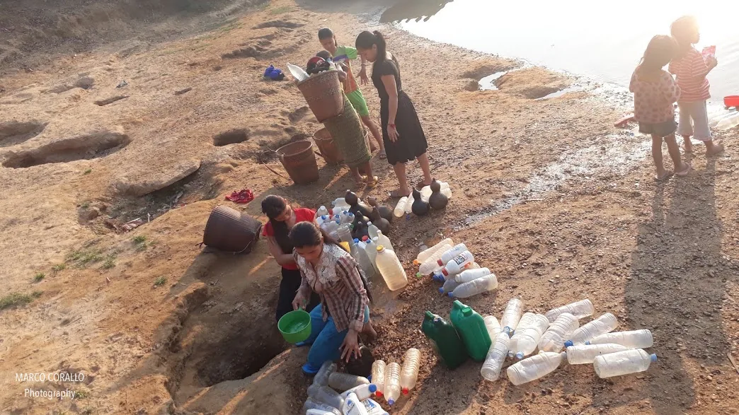 Le ragazzine di Koh Pek riempiono bottiglie e secchi d'acqua da un pozzo artigianale sulla riva del fiume