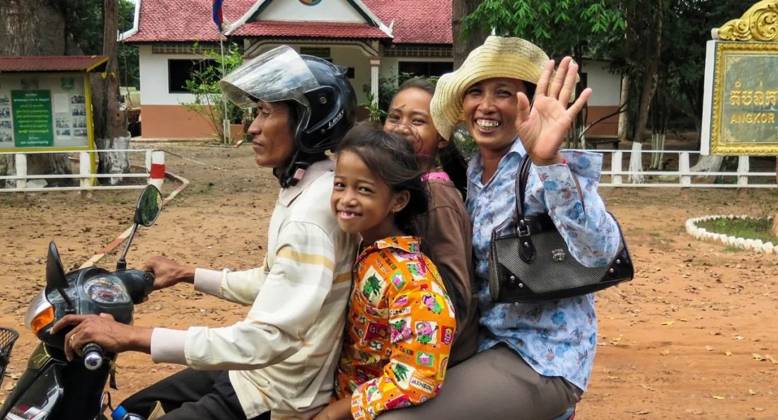 uno scooter con 4 passeggeri: un uomo alla guida, due bambini nel mezzo e una donna che saluta sorridente