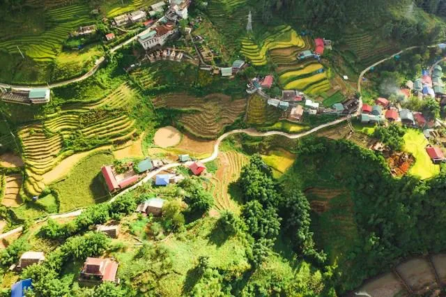 Vista aerea delle risaie a terrazze verdi con un villaggio di case dai tetti colorati nella valle tra le montagne